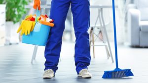 person with pail of cleaning supplies and broom
